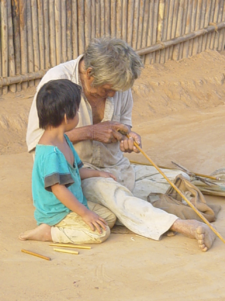 photo: Isho man makes an arrow as his grandson looks on